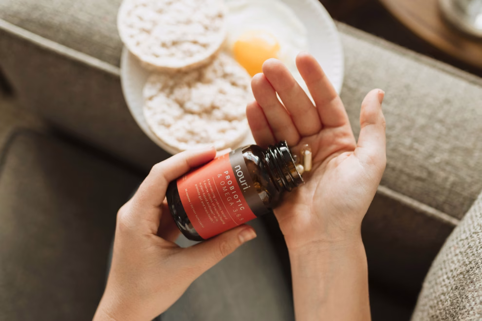 Saúde Suplementar Pessoa colocando na mão comprimidos de omega 3 com um prato no sofá, com o intuito de mostrar o suplemento.