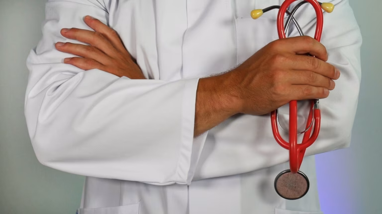 Auditoria em Planos de Saúde Médico, de jaleco branco, segurando equipamentos para ouvir o coração e examinar as pessoas.